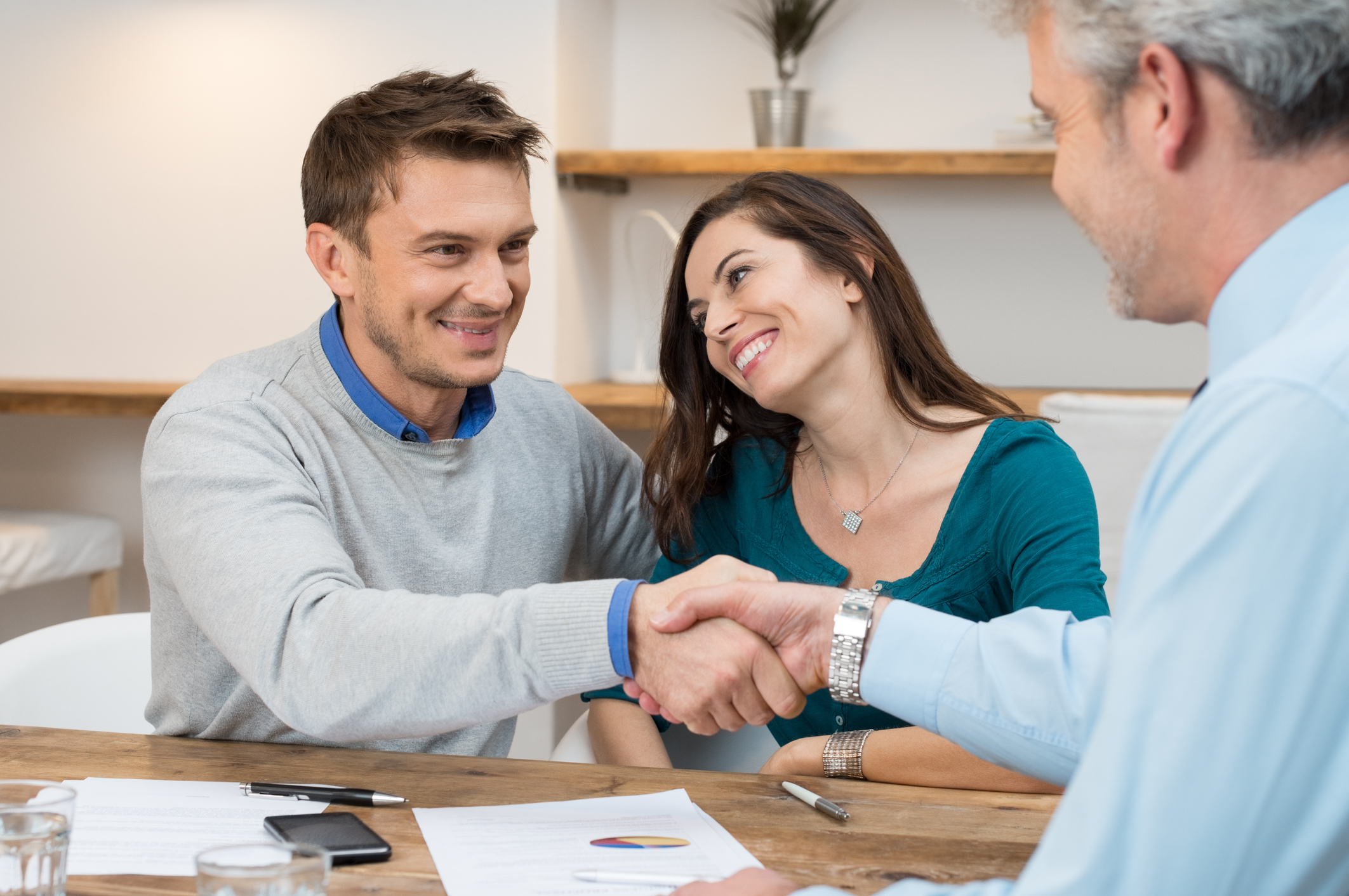 Couple sitting at a table in their home. The man is shaking the technician's hand that is sitting across the table from him, insinuating that they made a deal on a financing offer by Hales AC.